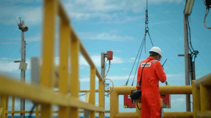 Um homem de macacão laranja trabalhando em uma plataforma de petróleo