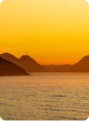 Imagem do mar, com montanhas ao redor ao pôr do sol