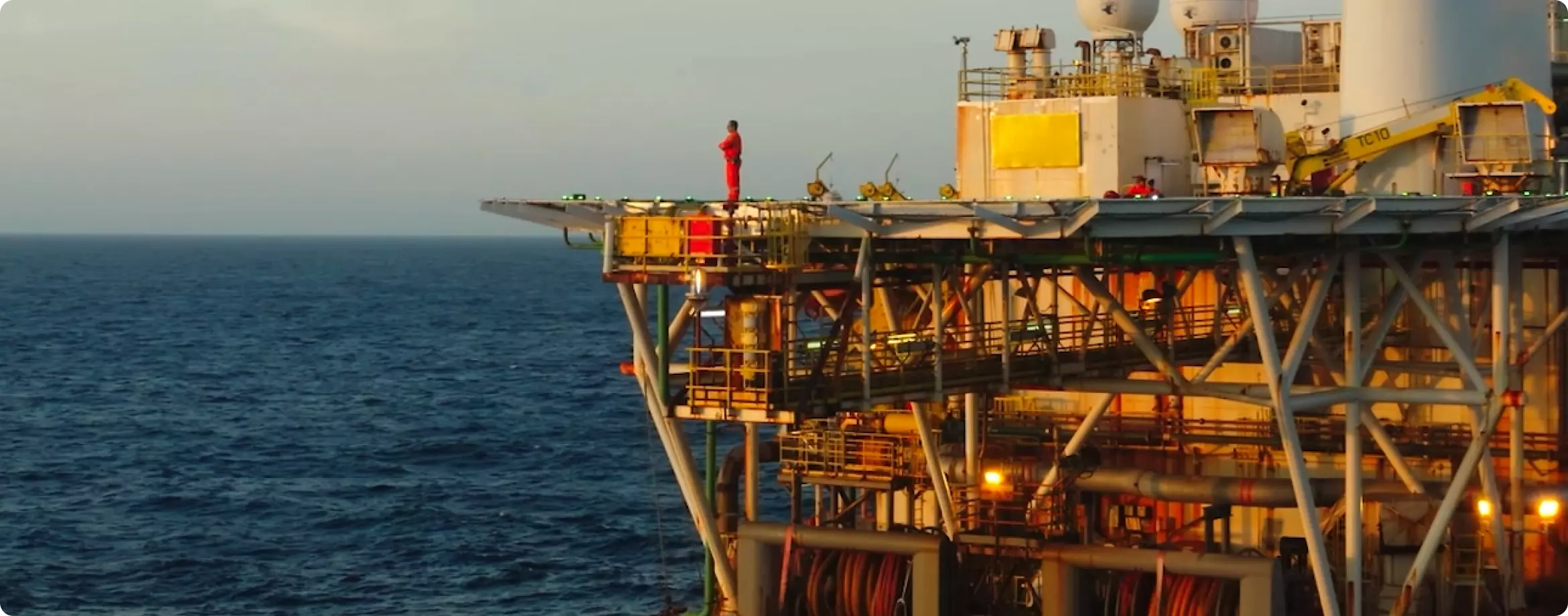 Imagem da ponta da plataforma de petróleo da PRIO com um trabalhador de pé nela observando o mar