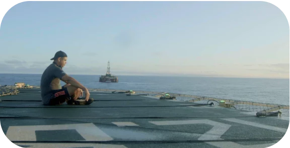 Um homem sentado em uma plataforma de petróleo observando o oceano